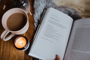 Photo of an open book on a fur rug with coffee cup and lit candle