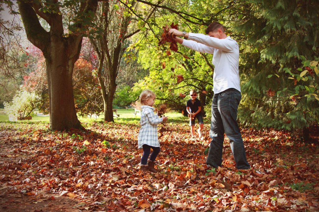 Father playing in autumn leaves with children