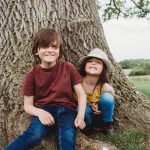 Young siblings sitting by a large tree