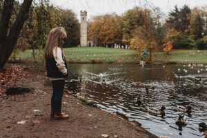 Young girl watching ducks in autumnal woodland
