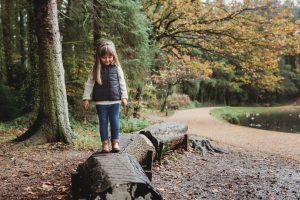 Young girl walking on tree trunks in autumnal woodland