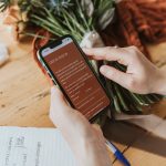 Photo of a female florist holding her phone, with the contact page of her website in focus.