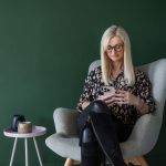 Relaxed photo of a business women sitting in a wingback chair reading emails with a coffee.