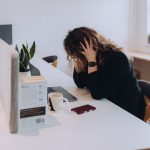 A female business owner holding her head whilst working at her desk.