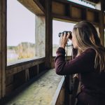 Photo of an artist bird watching outdoors in a bird hide with binnoculars.