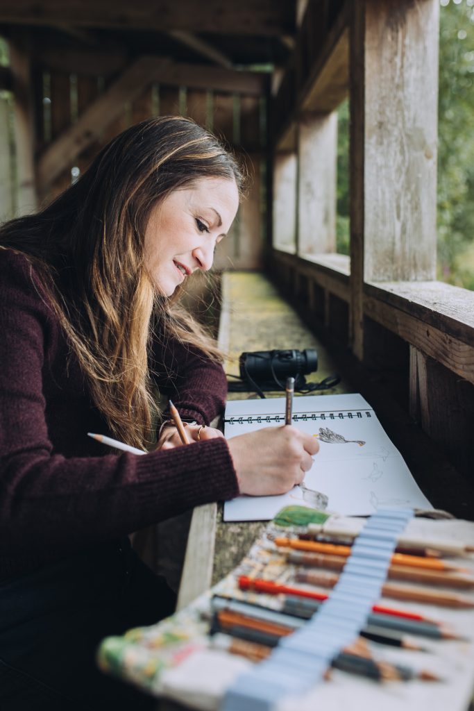 Portrait of a female artist sketching geese in a bird hide