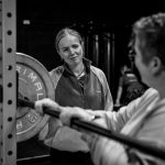 Black & white photo of a female personal trainer working in a gym with a client.