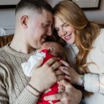 New parents holding their newborn baby at home on the sofa