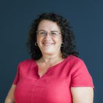 Studio headshot of a business women standing by a dark blue wall