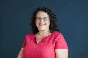 Studio headshot of a business women standing by a dark blue wall
