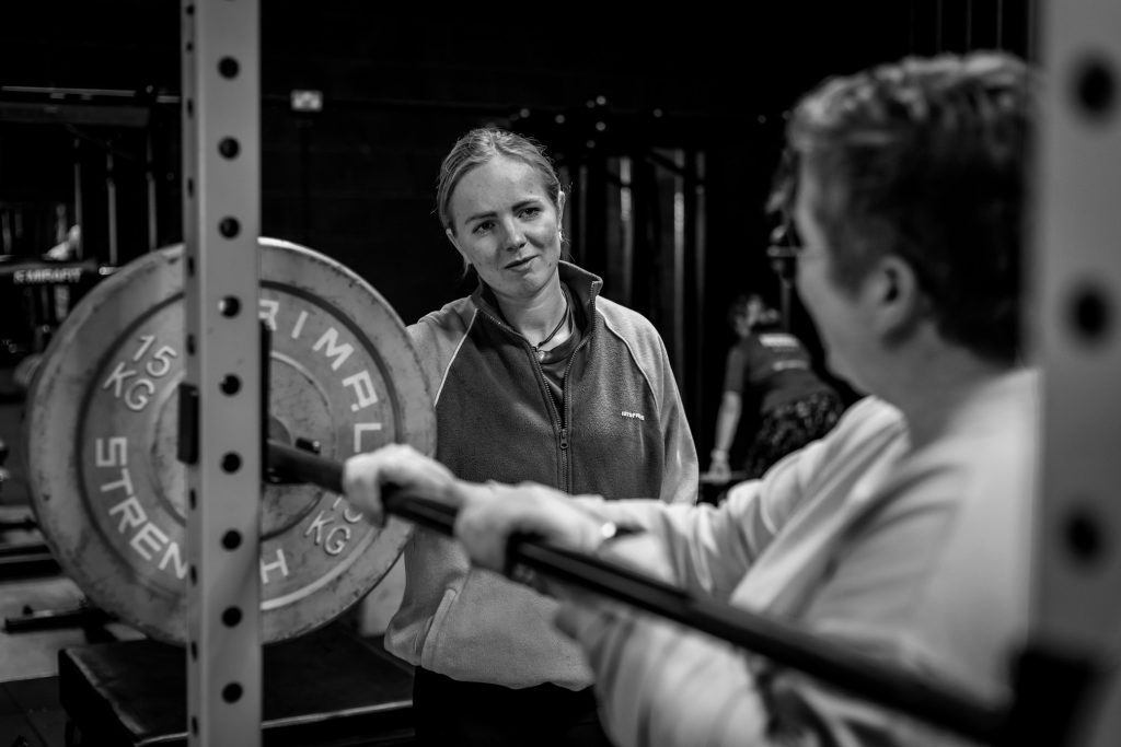 Black & white photo of a female personal trainer working in a gym with a client.