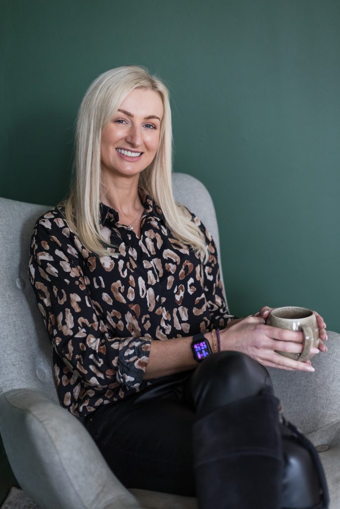 Relaxed photo of a business women sitting in a wingback chair with a coffee smiling at the camera