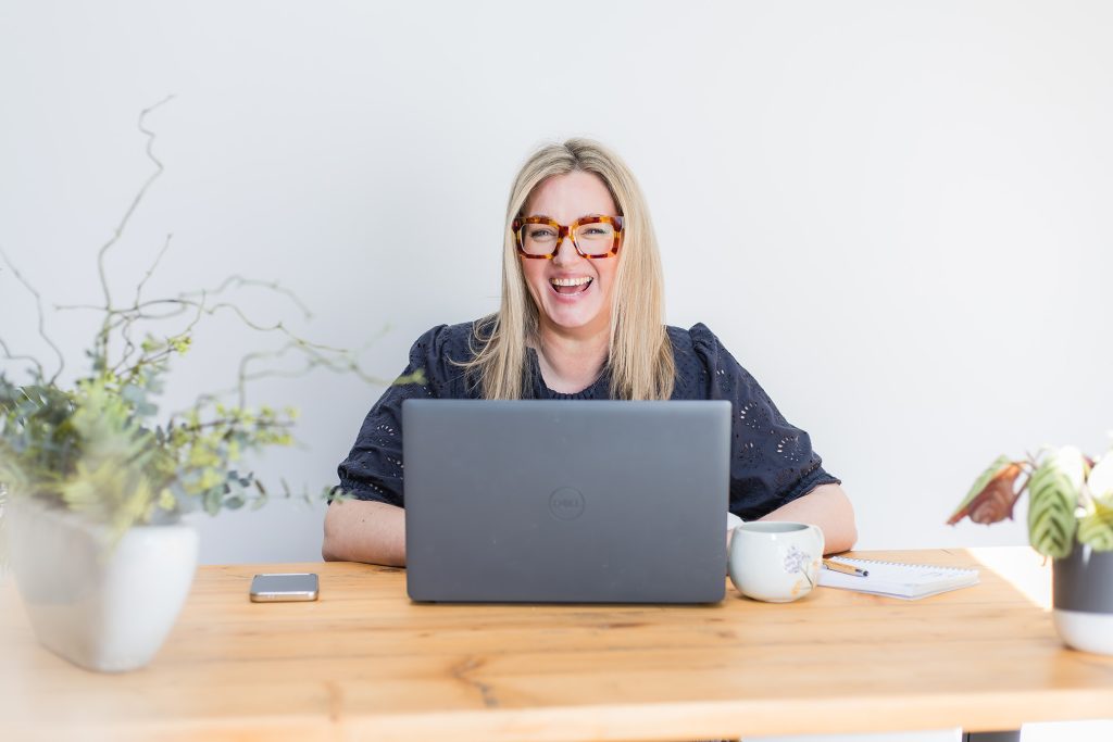 Photo of a woman laughing sitting at a desk with white wall behind her